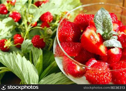 strawberries in a bowl and strawberries bunches. sliced ripe strawberries in a transparent bowl and strawberries bunches with leaves. Berry on the brown background