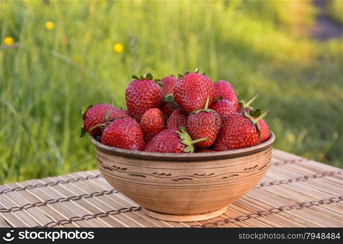 Strawberries in a clay bowl on a sunny day on the mat. Strawberries in a clay bowl