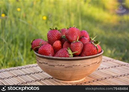 Strawberries in a clay bowl on a sunny day on the mat. Strawberries in a clay bowl