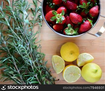strawberries in a colander, herbs, and lemons on a wood cutting board