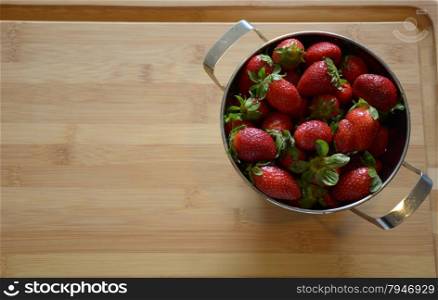 strawberries in a colander on a wood cutting board