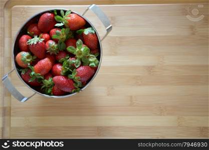strawberries in a colander on a wood cutting board