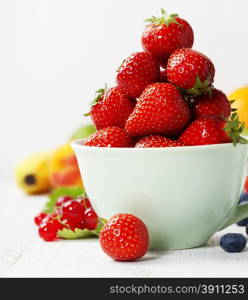 Strawberries in a cup and fresh fruits on rustic background