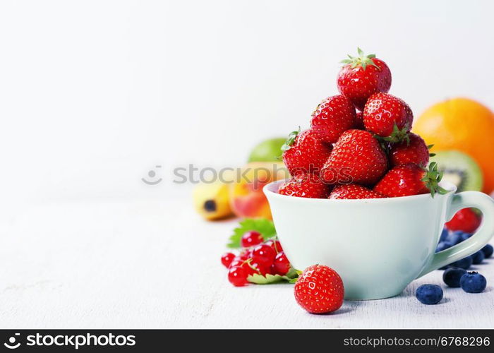 Strawberries in a cup and fresh fruits on rustic background