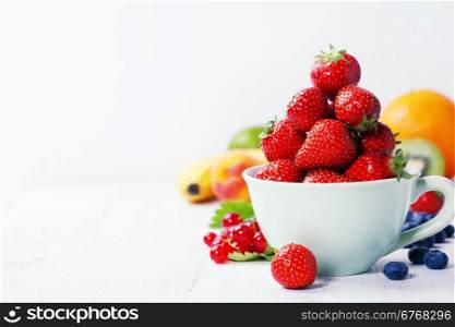 Strawberries in a cup and fresh fruits on rustic background