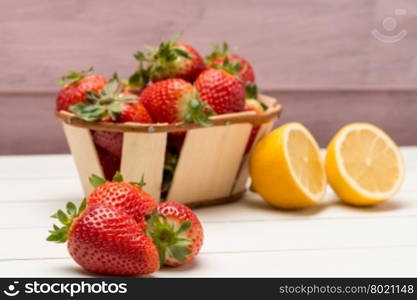 Strawberries in a small basket and lemon on wooden table.