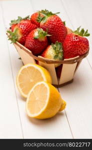 Strawberries in a small basket and lemon on wooden table.