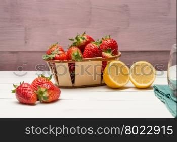 Strawberries in a small basket and lemon on wooden table.