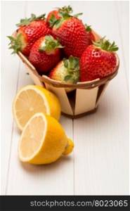 Strawberries in a small basket and lemon on wooden table.