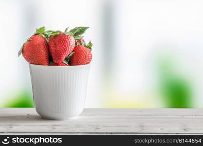 Strawberries in a white cup on a wooden table