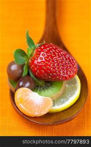 Strawberries, kiwi, mandarin orange, lemon and chocolate candy in the wooden spoon of the orange fabric