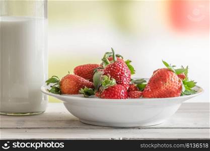 Strawberries on a plate with a bottle of milk on a table