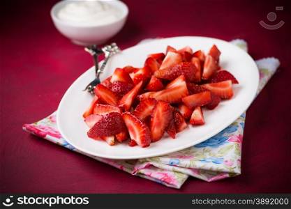 Strawberries on plate with cream over red background, selective focus
