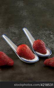 Strawberries on sugar in spoons with a slate background