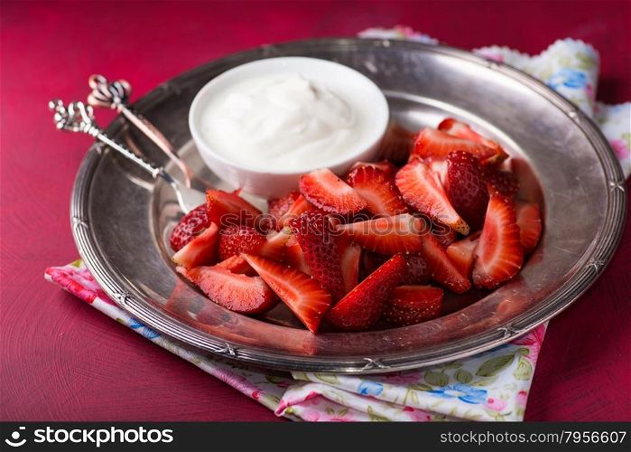 Strawberries on vintage plate with cream over red background, selective focus