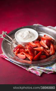 Strawberries on vintage plate with cream over red background, selective focus, copy space