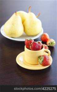 strawberries, pears on a plate and cup with saucer on a wooden table