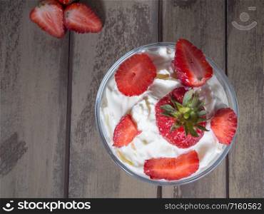 Strawberries with whipped cream in a glass bowl on wooden background. Top view. Ice cream with fresh strawberries. Top view