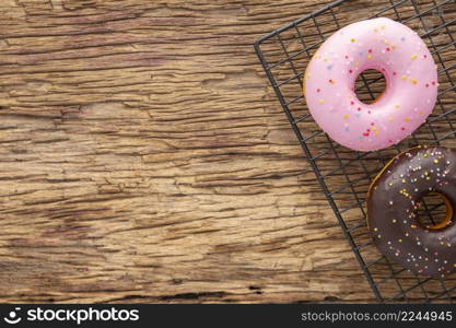 strawberry and chocolate donut with sprinkles in black cooling rack grid on rustic natural wood texture background with copy space for text, brown tone, top view