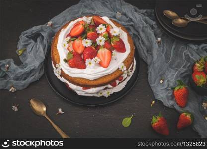 Strawberry cake, strawberry sponge cake with fresh strawberries and sour cream on a dark kitchen countertop.