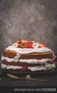 Strawberry cake, strawberry sponge cake with fresh strawberries and sour cream on a dark kitchen countertop.