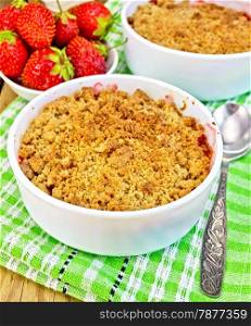 Strawberry crumble in a white bowl, spoon on green napkin, strawberries on a wooden boards background
