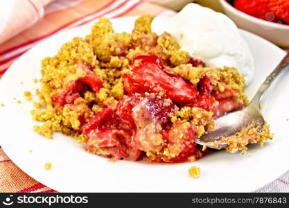 Strawberry crumble in plate with a spoon on a napkin, strawberries on a wooden boards background