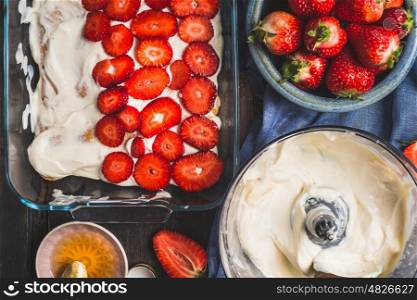 Strawberry dessert making. Dish with sliced berries and cream on dark rustic background, top view