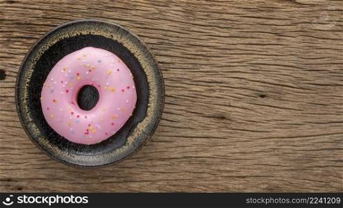 strawberry donut with sprinkles in ceramic plate on rustic natural wood texture background with copy space for text, top view