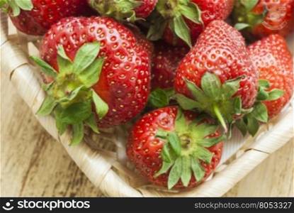 Strawberry fruit lying in basket. The view from the top.. Strawberry fruit lying in a wicker basket. The basket stands on a weathered Board.