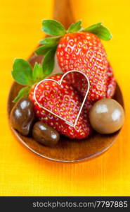 strawberry, hearts and chocolate candy in the wooden spoon of the orange fabric