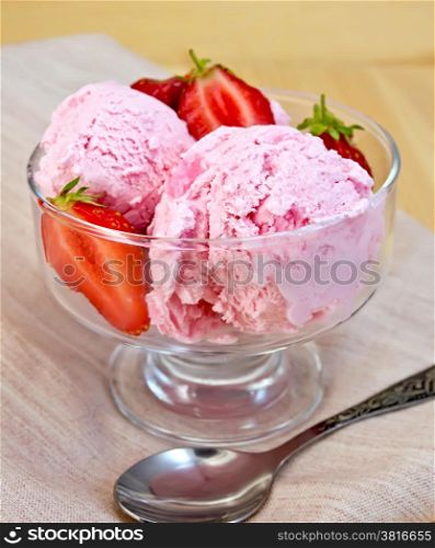 Strawberry ice cream in a glass bowl with strawberries, spoon on a napkin on a wooden boards backgrou