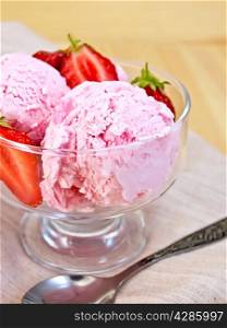 Strawberry ice cream in a glass bowl with strawberries, spoon on a napkin on a wooden board