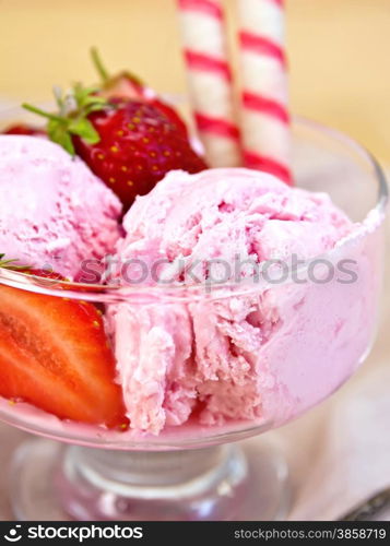 Strawberry ice cream in a glass bowl with wafer rolls and strawberries, napkin on a wooden boards background