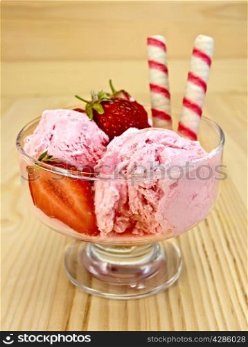 Strawberry ice cream in a glass bowl with wafer rolls and strawberries on a wooden boards background