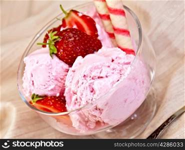 Strawberry ice cream in a glass bowl with wafer rolls and strawberries, spoon on a cloth background
