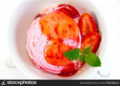 Strawberry ice cream in a white bowl with strawberries, mint and strawberry syrup on the background light wooden boards on top