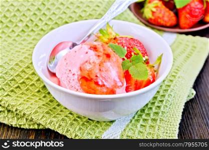 Strawberry ice cream in a white bowl with strawberries, strawberry syrup and a spoon on a napkin on a wooden boards background