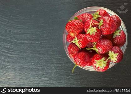 Strawberry in a bowl on a black slate table. Top view, flat lay, mockup with copy space for text. Strawberry in a bowl on black backround