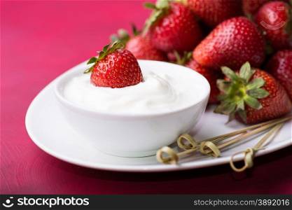 Strawberry in a bowl with cream over red background, selective focus