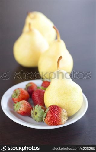 strawberry in plate, pear and peach on a wooden table