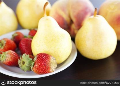 strawberry in plate, pear and peach on a wooden table