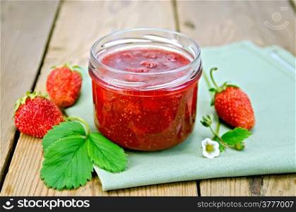 Strawberry jam in a glass jar, berry, leaf and flower strawberry, napkin on background of wooden boards