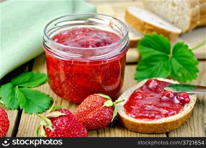 Strawberry jam in a glass jar, bread, strawberry with leaves, napkin, knife on background wooden plank