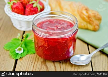 Strawberry jam in a glass jar, layered bun, strawberries in a basket, napkin, spoon on a wooden board