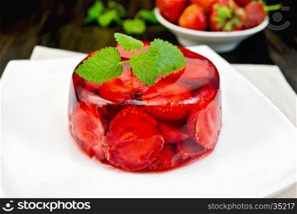 Strawberry jelly with mint and berries in a plate on a towel on the background of dark wood planks