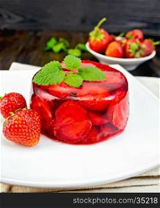 Strawberry jelly with mint and berries in a plate on a towel on the background of wooden boards