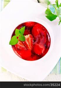 Strawberry jelly with mint and berries in white plate on the kitchen towel on a background of wooden boards on top