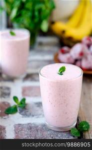 Strawberry, milk and banana smoothie or milkshake in a glass, decorated with a mint leaf. Selective focus on mint. Healthy food or snacks, close-up