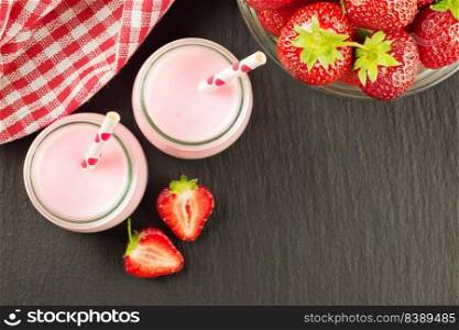 Strawberry milkshake in the glass jar with drinking straw on black slate background. Top view, flat lay, mockup with copy space for text. Strawberry milkshake in the glass jar on blue wooden background